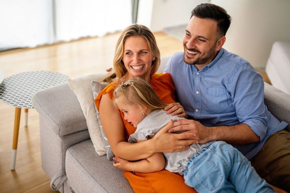 Three people smiling on a couch, with a child resting in a woman’s lap