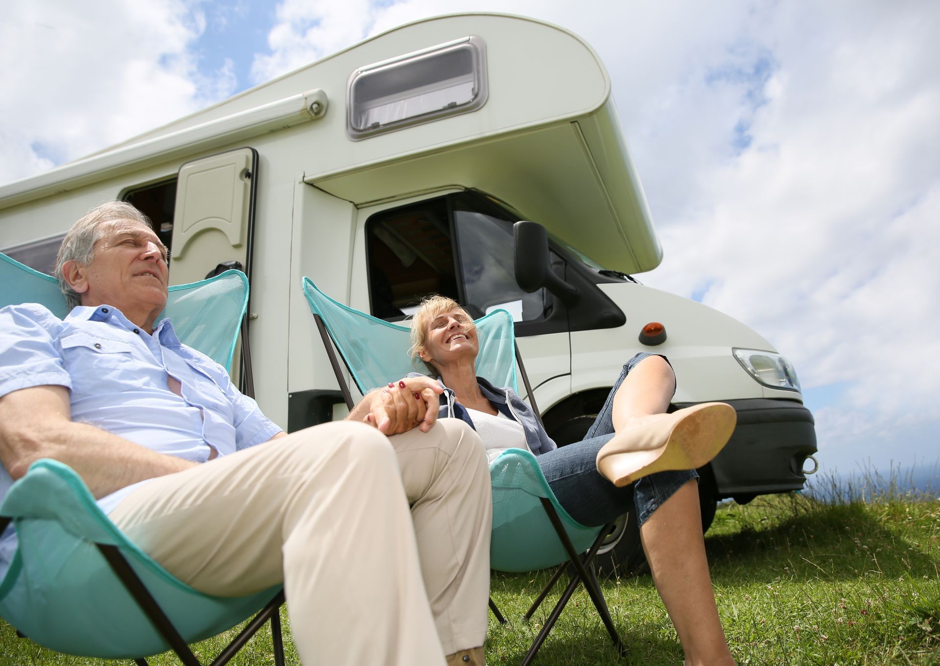 Two people relaxing in folding chairs outside a green camper under a blue sky