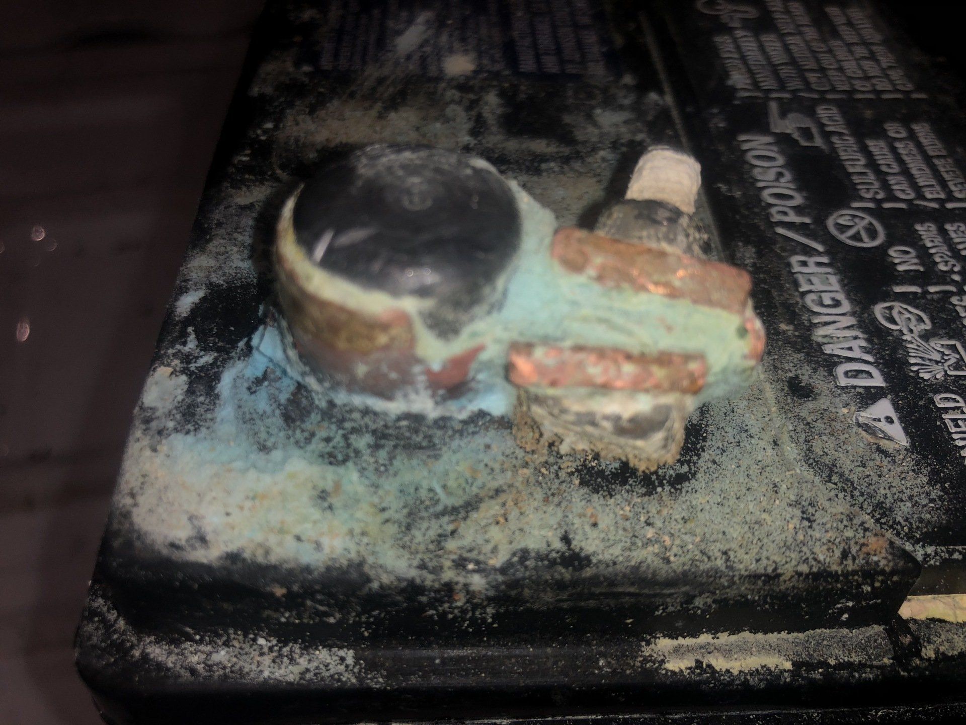 Corroded car battery terminal covered in blue-green and white residue.