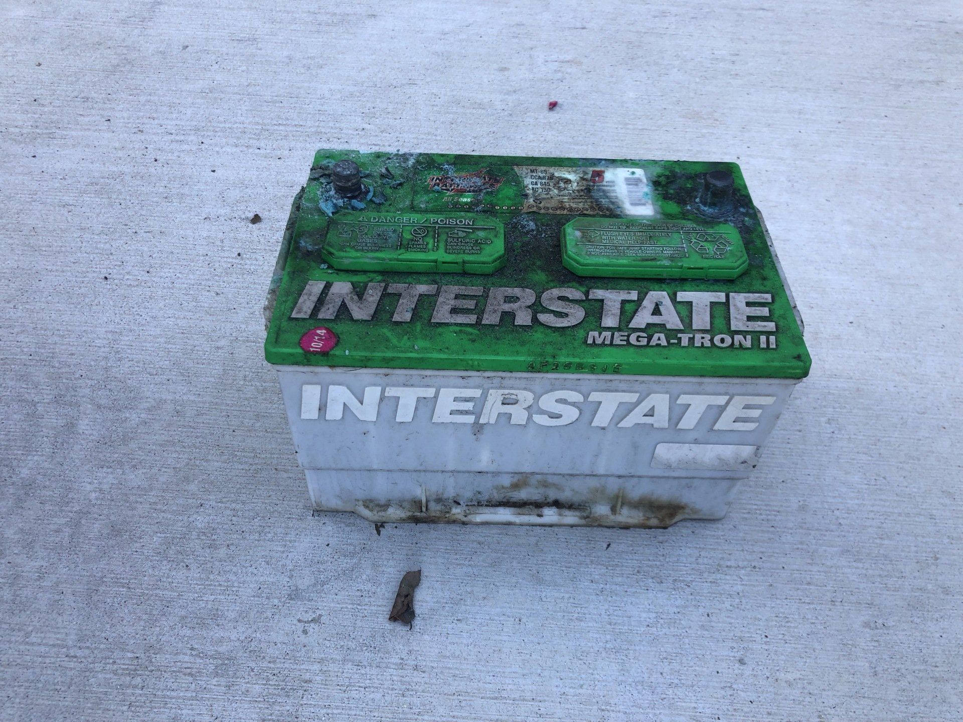 An Interstate car battery on a concrete surface. The battery is green and white with corrosion.