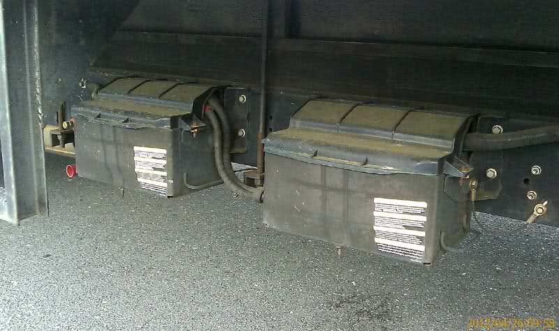 Two black rectangular boxes, likely batteries, on a black surface. Cables connect them.