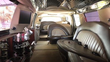 Interior of a limousine with tan and brown seating, a TV, and a bar area.