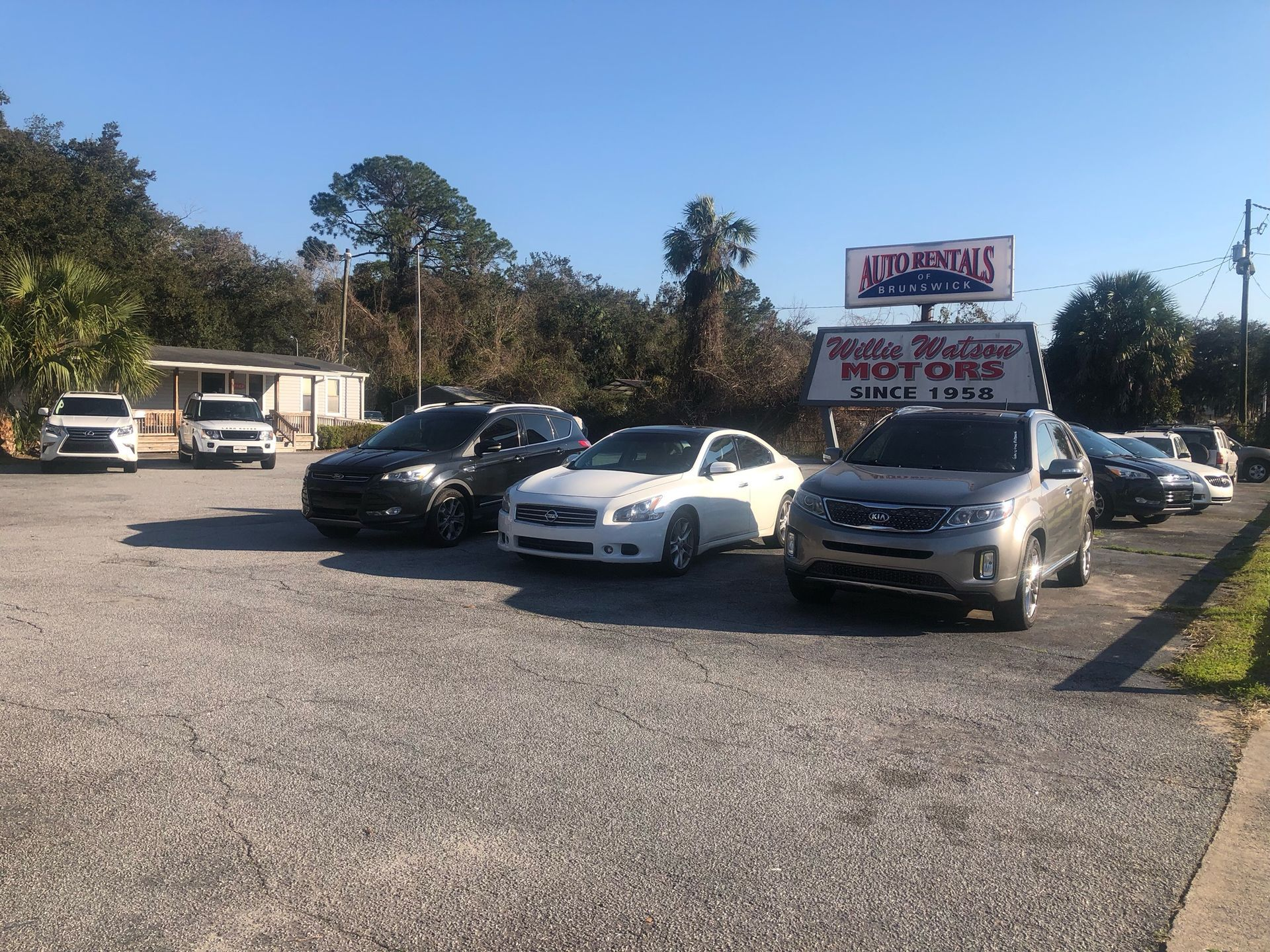 A car dealership with cars parked on gravel, sign for White Motors visible on a sunny day.