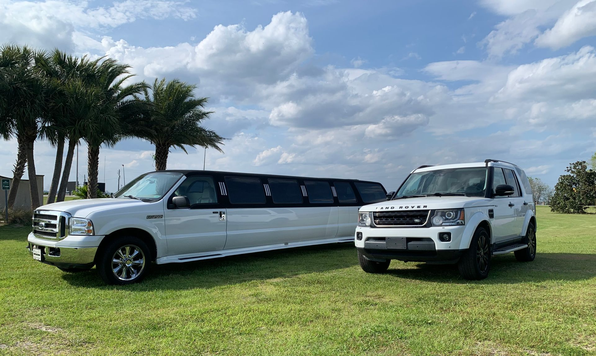 White limousine and SUV parked on a grassy field under a cloudy sky.