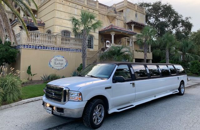 White limousine parked in front of a beige building with a tiled facade, likely a hotel or event venue.