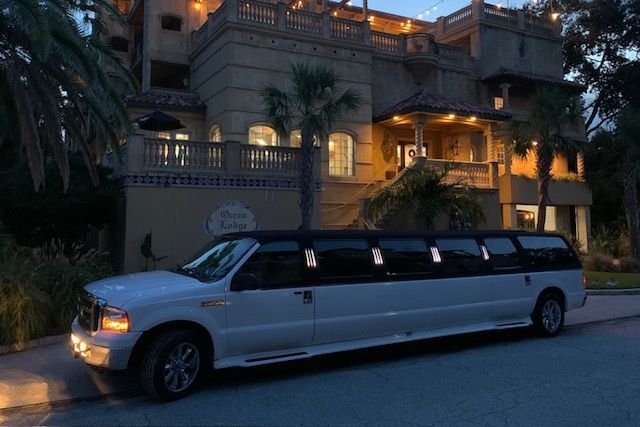 White limousine parked in front of a large, ornate building with lights on at dusk.