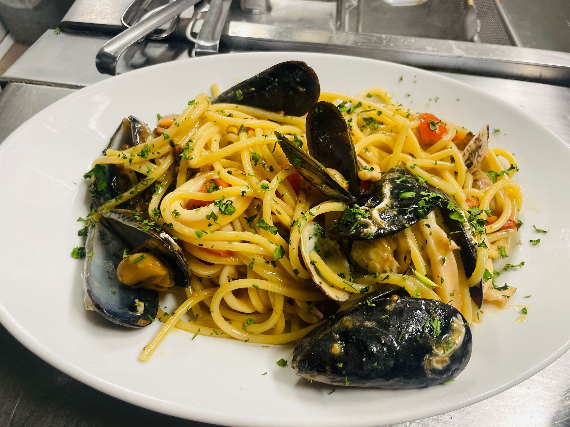 Spaghetti con cozze, vongole ed erbe aromatiche su un piatto bianco in cucina.