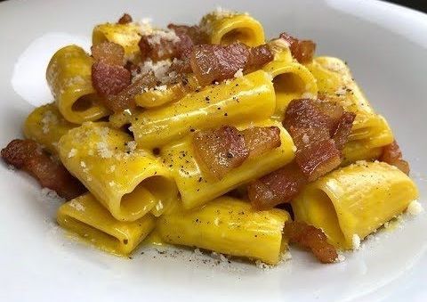 Pasta alla carbonara con rigatoni, pancetta e formaggio su un piatto bianco.
