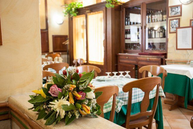 Interno di un ristorante con tavoli apparecchiati per cenare, fiori e mobili in legno.