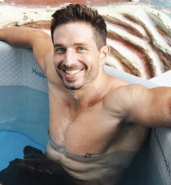 Man with dark hair smiles, relaxing in a hot tub.