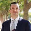 Woman smiling, wearing white shirt and black skirt, arm on hip, outdoors.