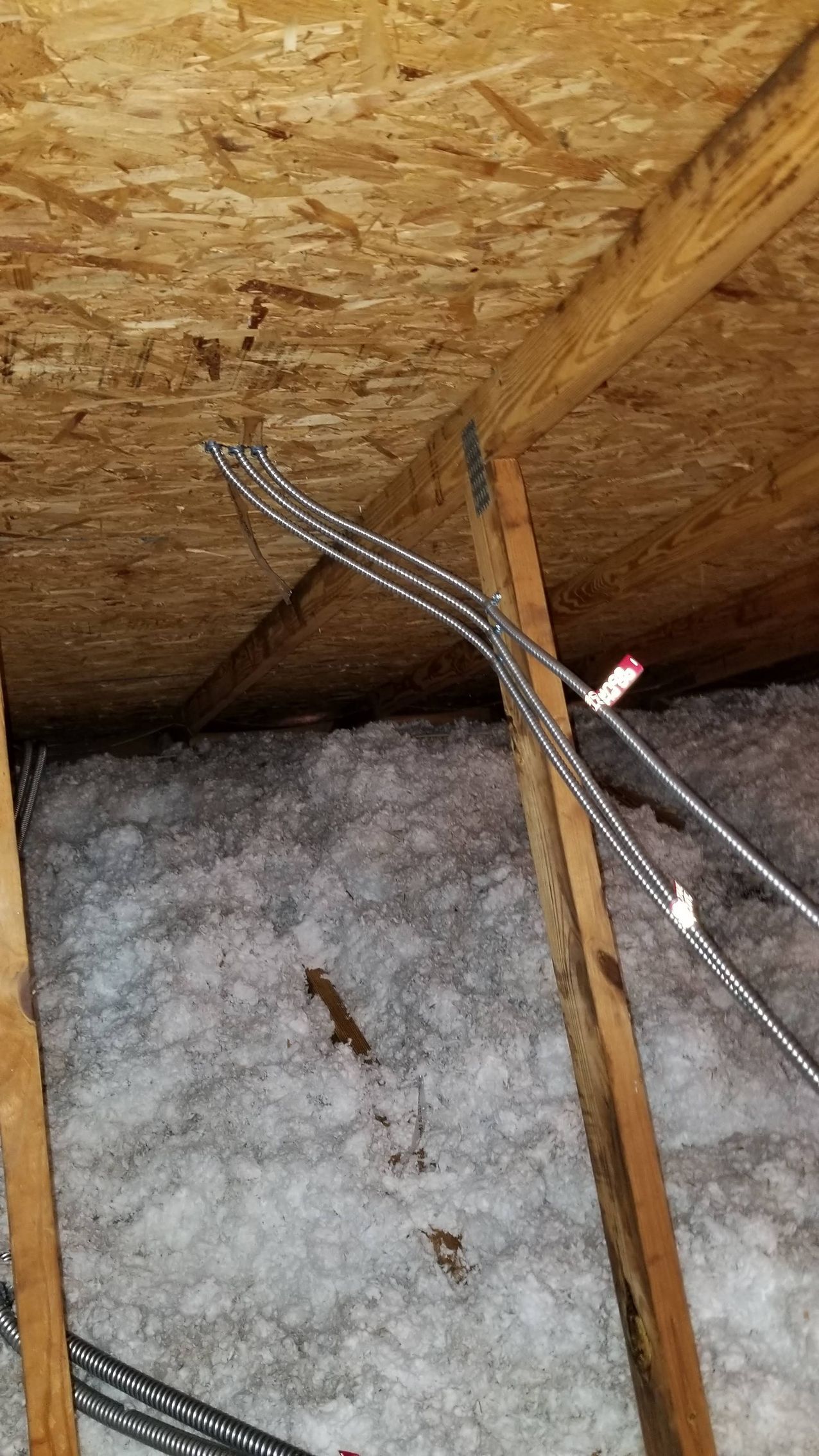 A bunch of wires are hanging from the ceiling of an attic.