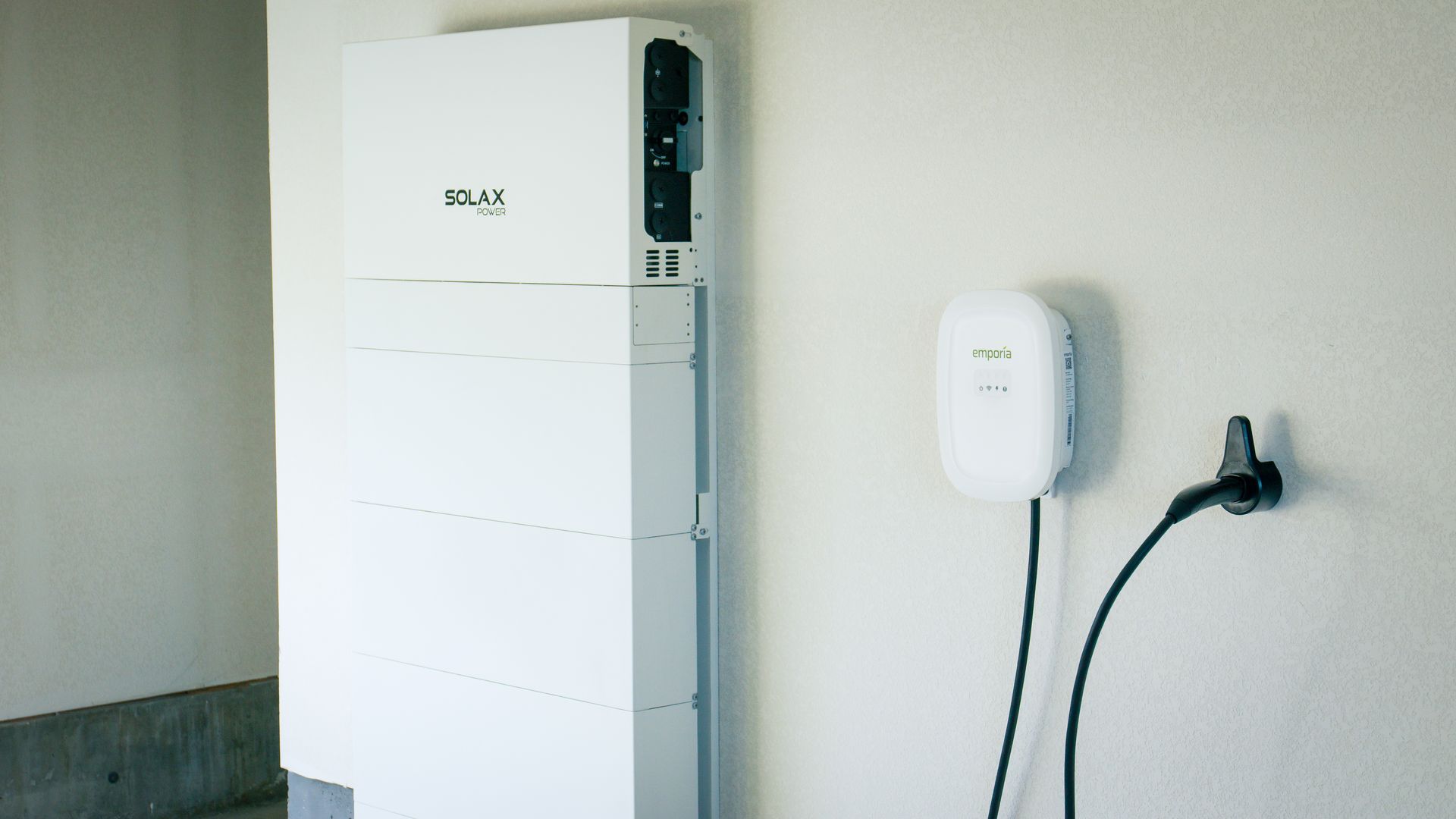 A white box is sitting on a white wall next to a charger.