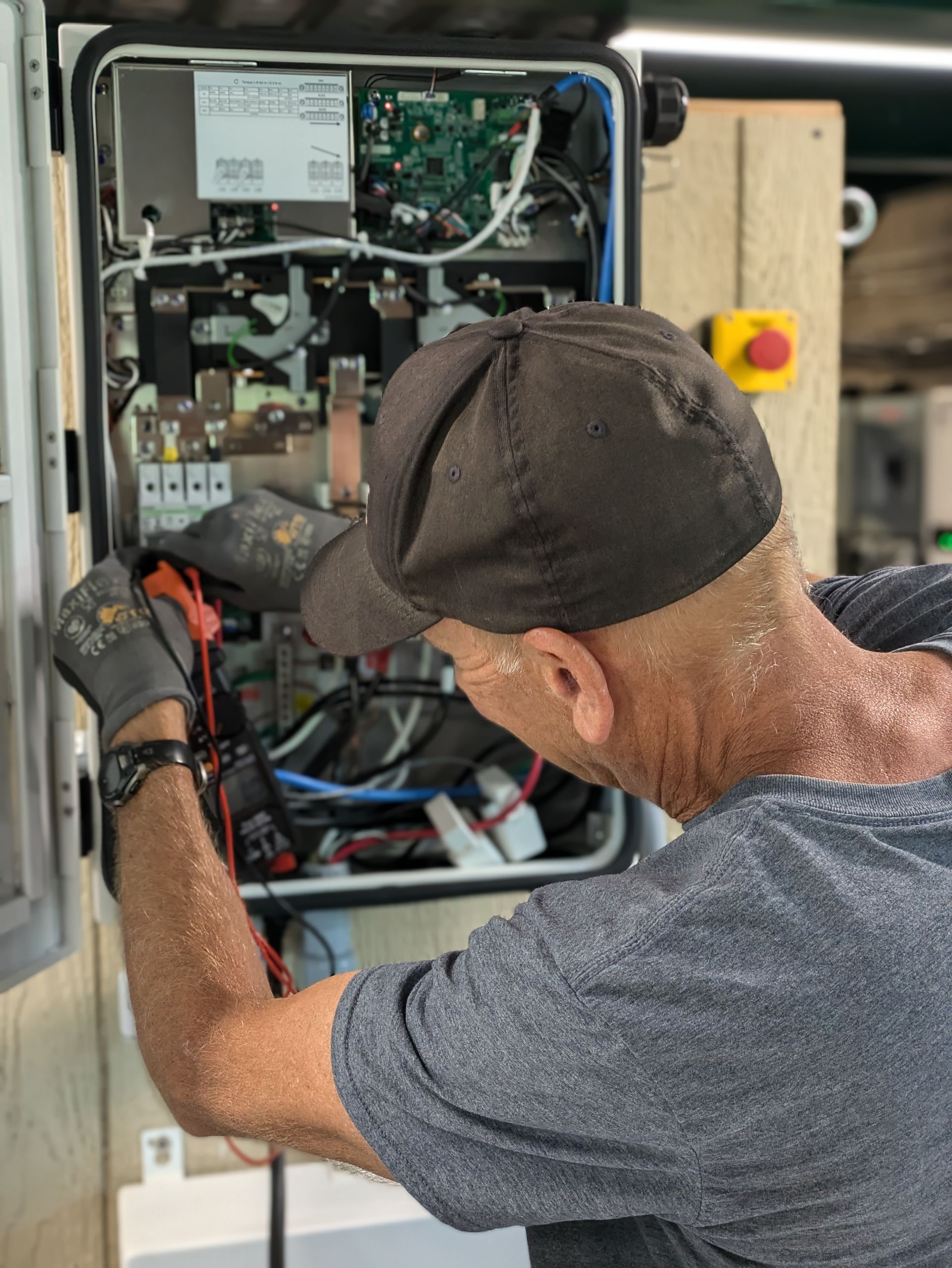 A man in a baseball cap is working on a electrical box.