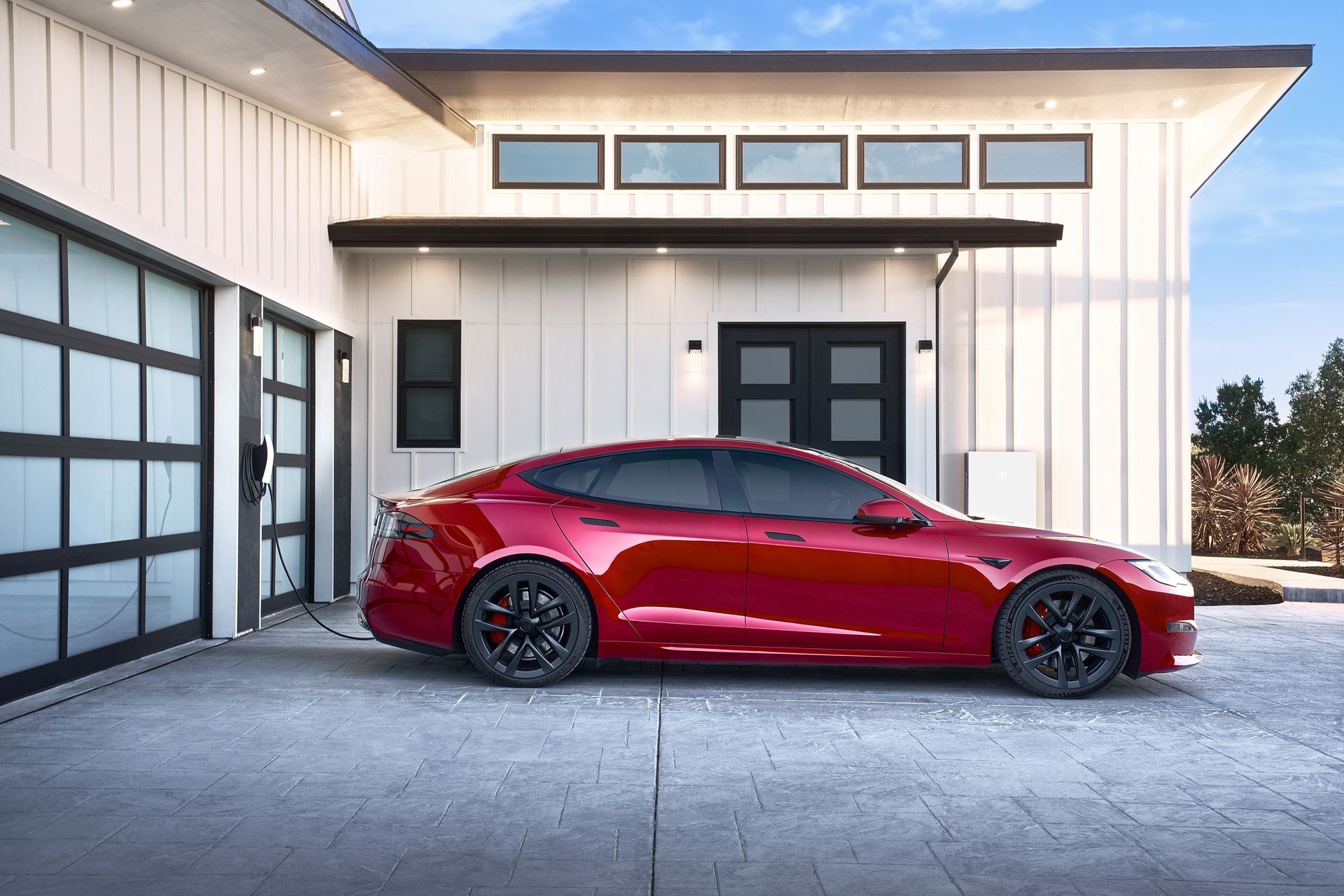 A red tesla model s is parked in front of a white house.
