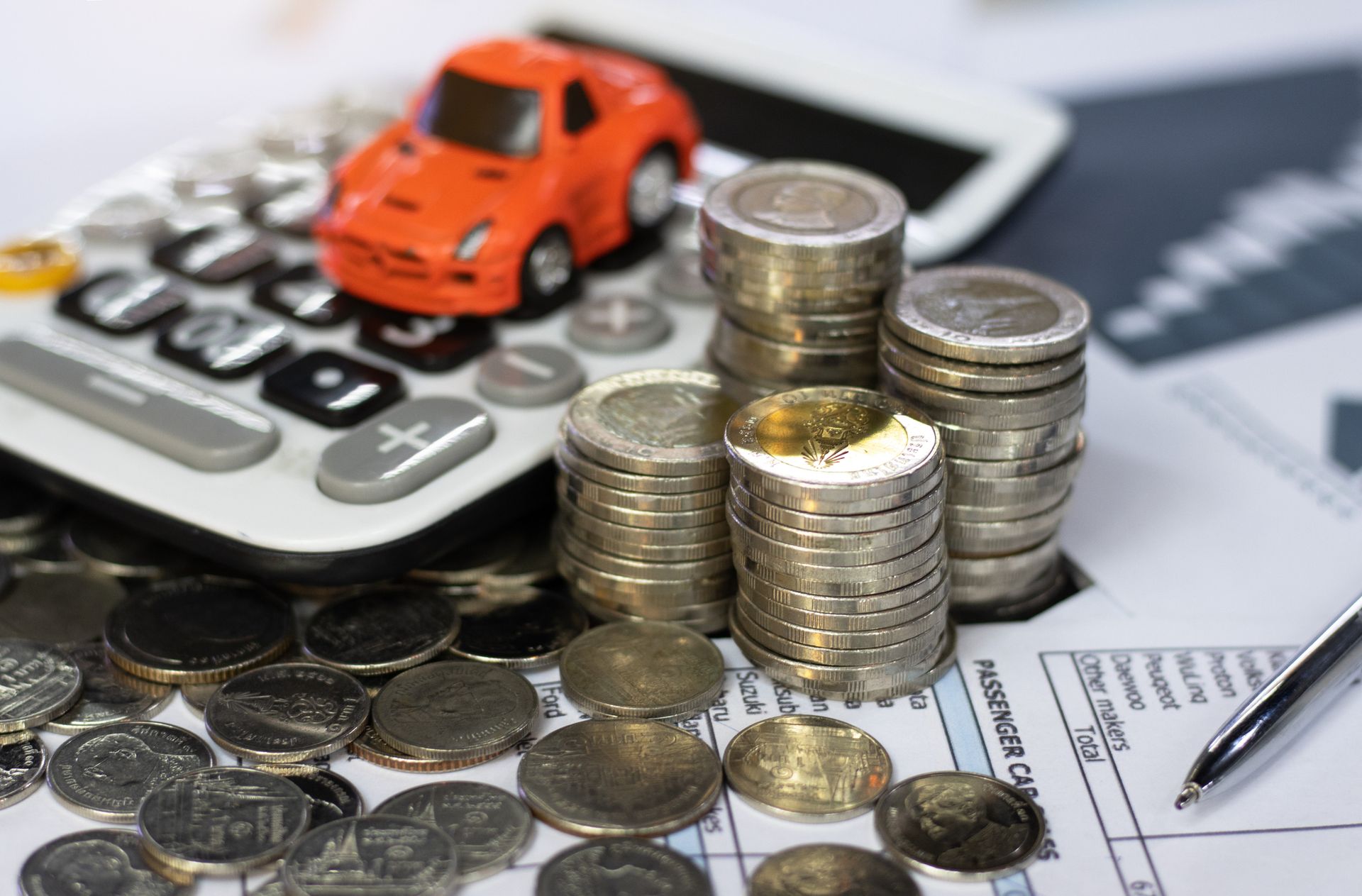 A toy car is sitting on top of a pile of coins next to a calculator.
