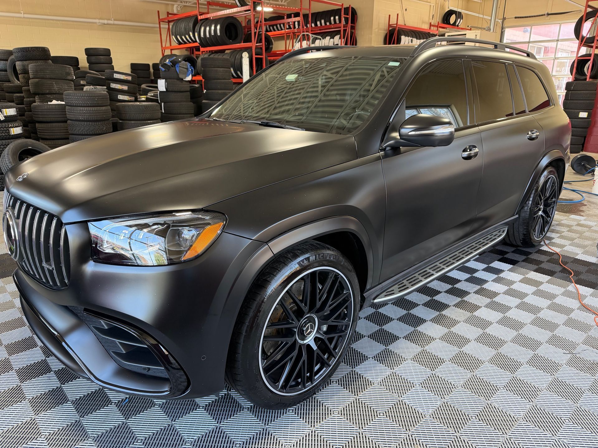 Matte black SUV in a garage, shown from the front side on a checkered metal floor