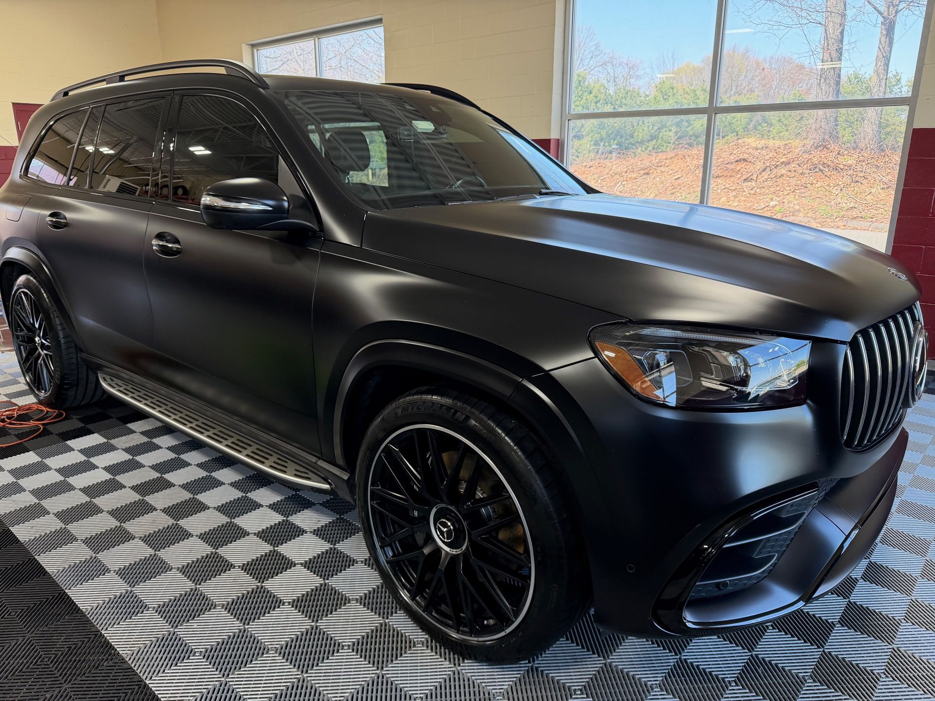 Matte black SUV parked indoors on a checkered floor near large windows.