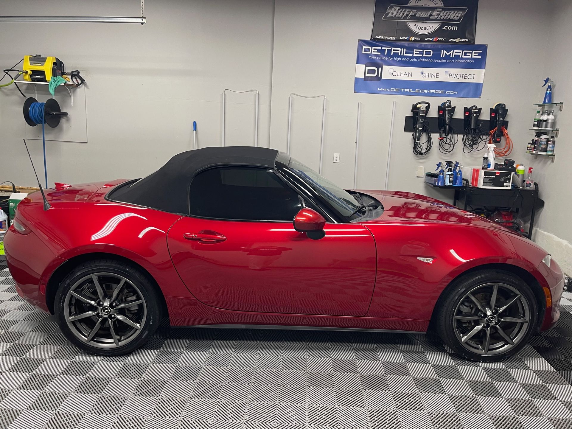 Red Mazda convertible parked inside a garage, next to detailing supplies.