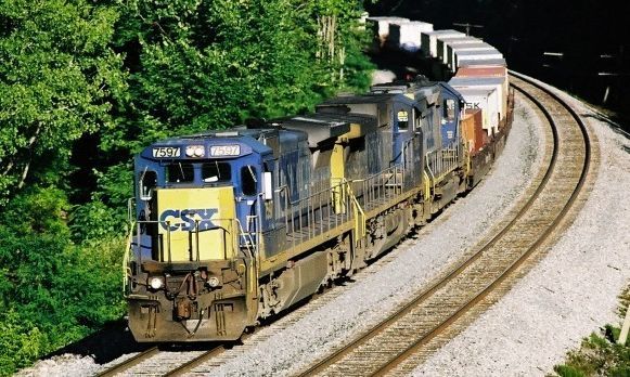 A CSX train on curved tracks surrounded by trees. Blue and yellow engine leads.