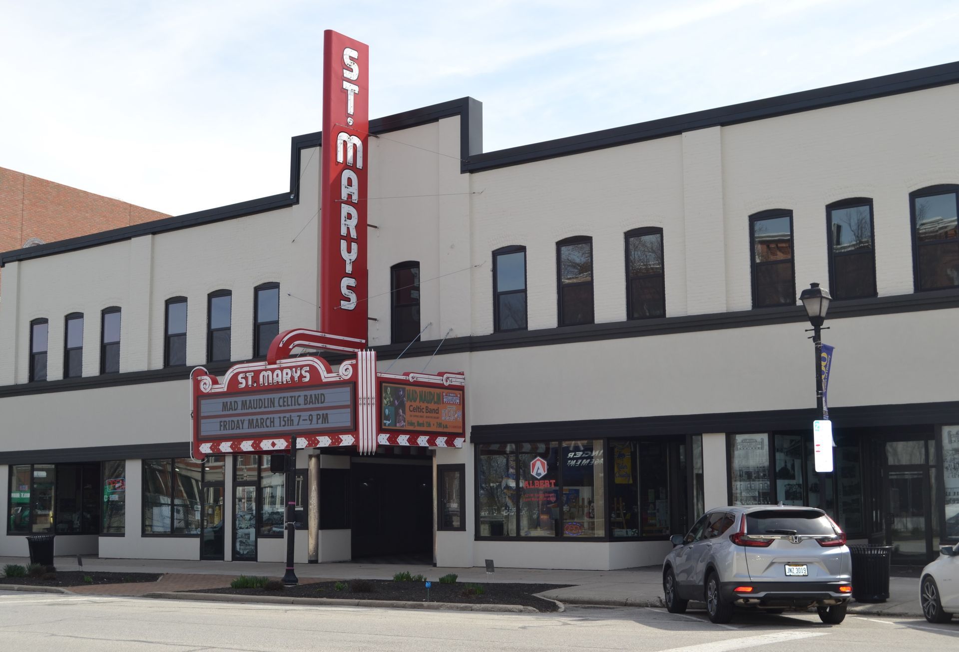 St. Marys Theatre, brick building with red neon sign. Car parked out front, sidewalk view.