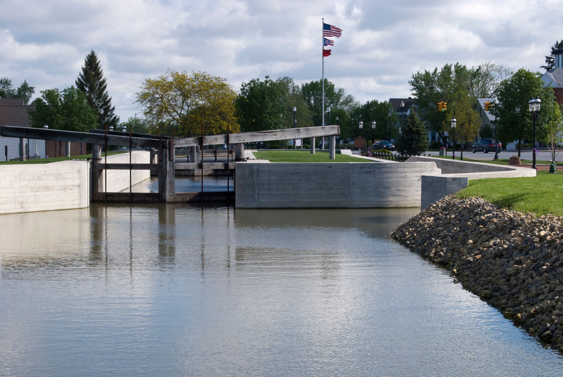 Water canal with concrete structures and three flags waving in the background.