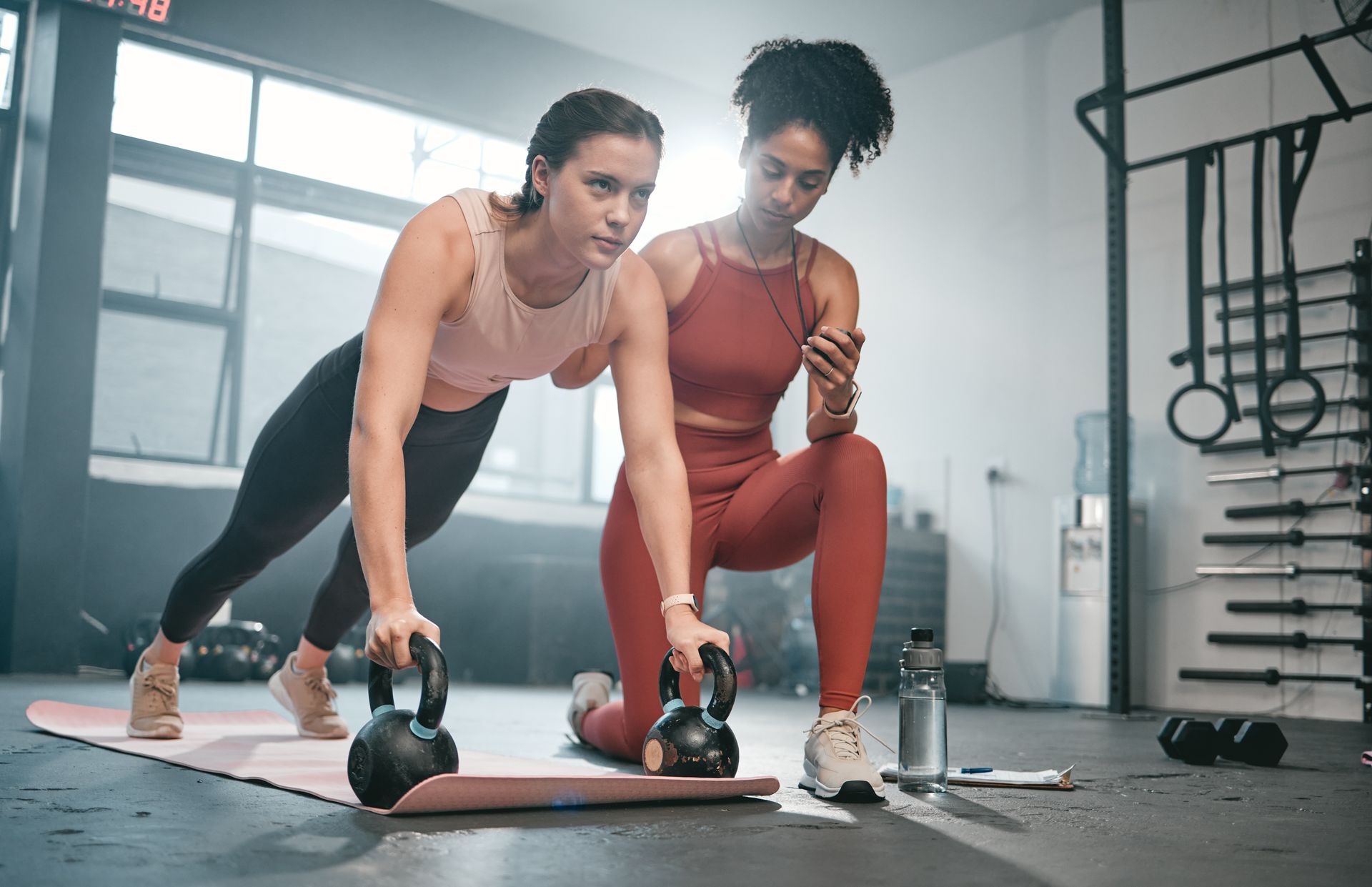 Trainer assisting woman stretching in a bright gym with yoga blocks and exercise mats