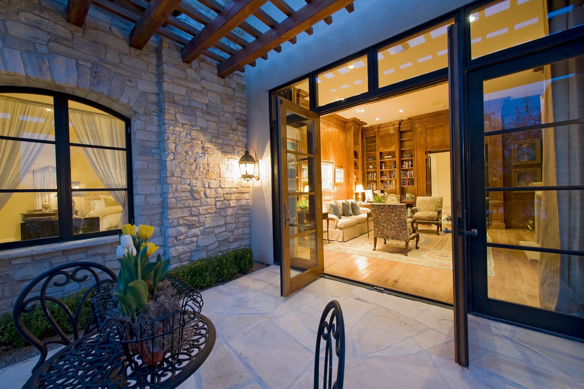 Stone patio with open French doors leading to a warmly lit home interior at dusk Stone patio with open French doors leading to a warmly lit home interior at dusk