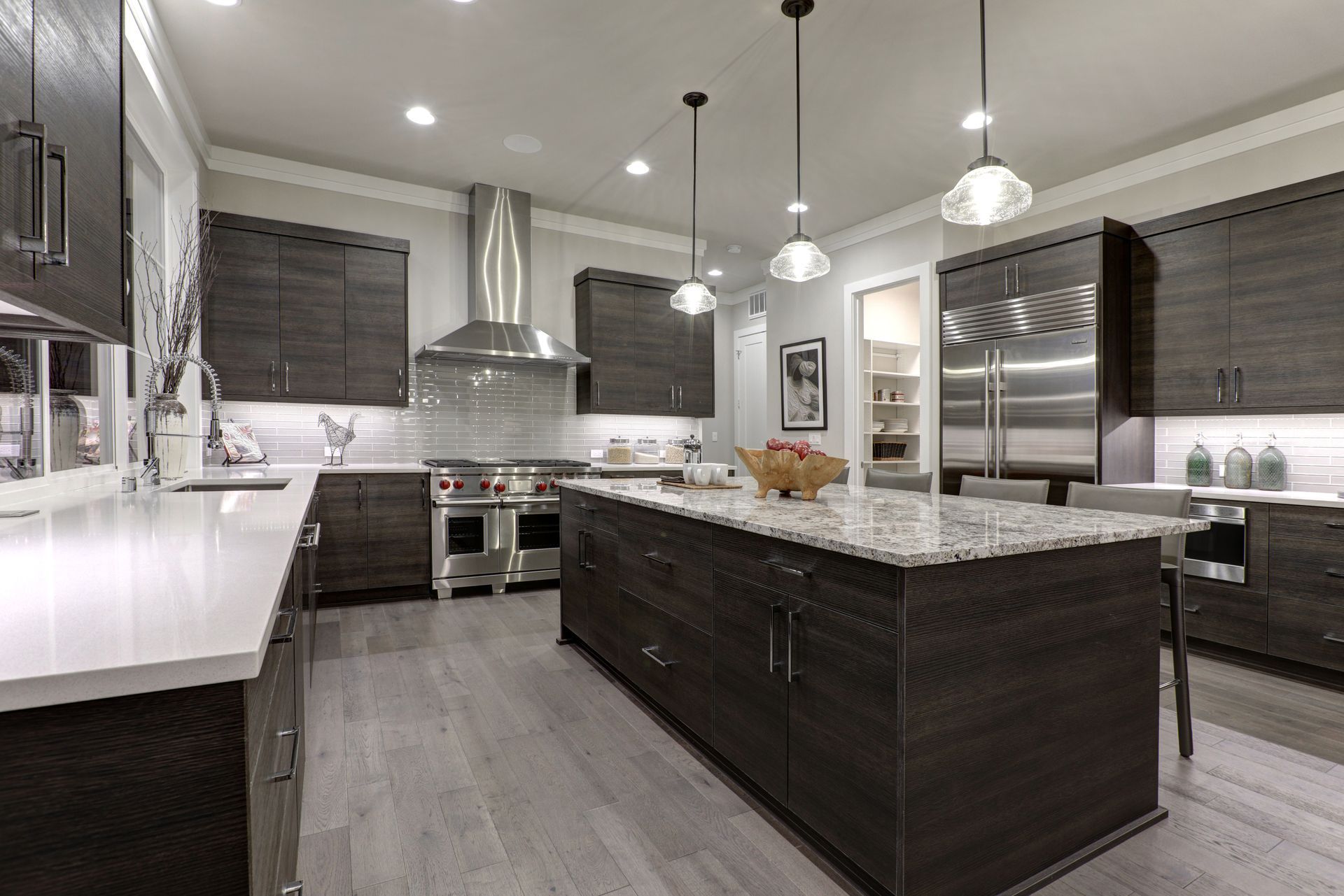 Modern kitchen with dark island, stainless steel appliances, white counters, and pendant lights Modern kitchen with dark island, stainless steel appliances, white counters, and pendant lights