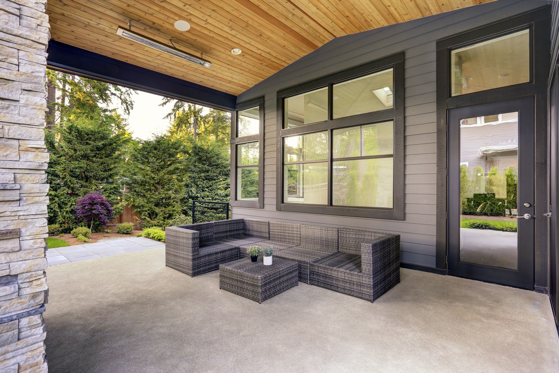 Covered patio with wicker seating, large windows, and a wood-paneled ceiling