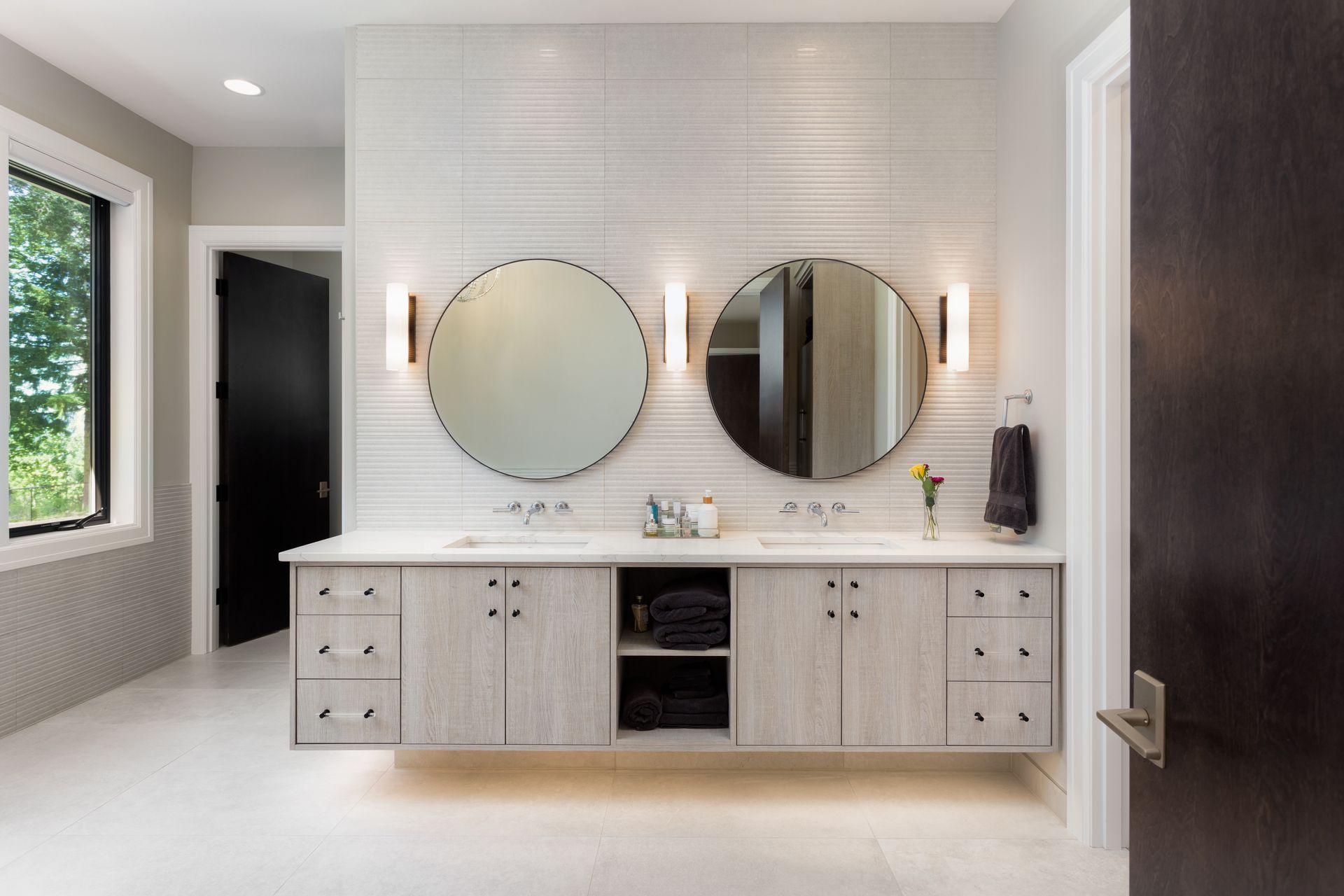 Modern bathroom vanity with two round mirrors, white cabinetry, and dark wood doors.