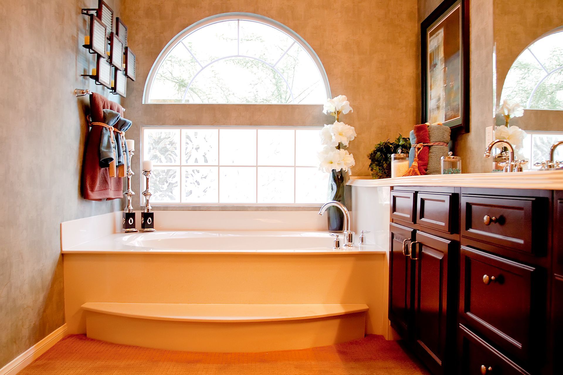 Elegant bathroom with a corner soaking tub, arched window, and dark wood vanity under warm light Elegant bathroom with a corner soaking tub, arched window, and dark wood vanity under warm light