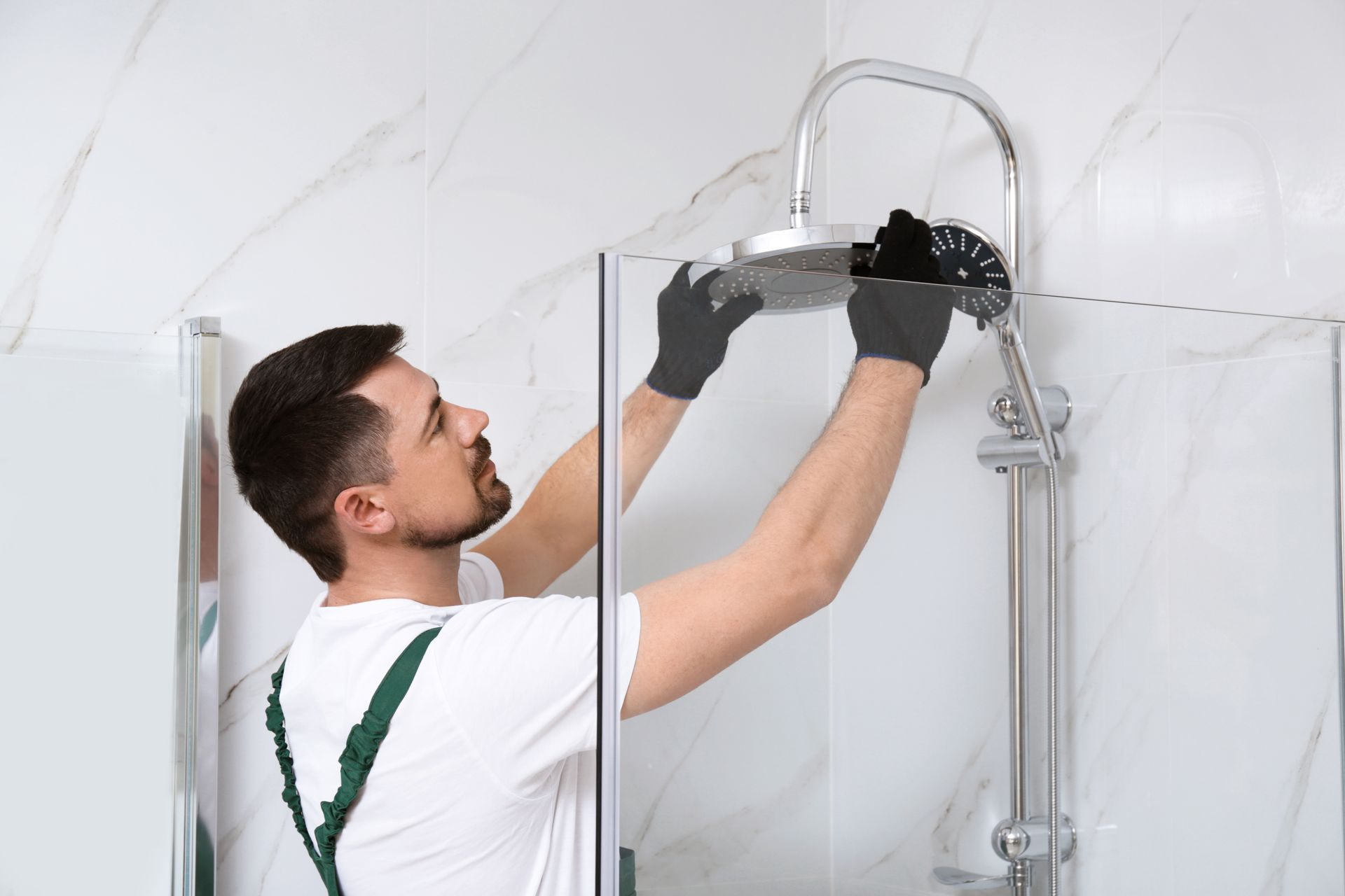 Worker installing a glass shower door with a drill in a tiled bathroom