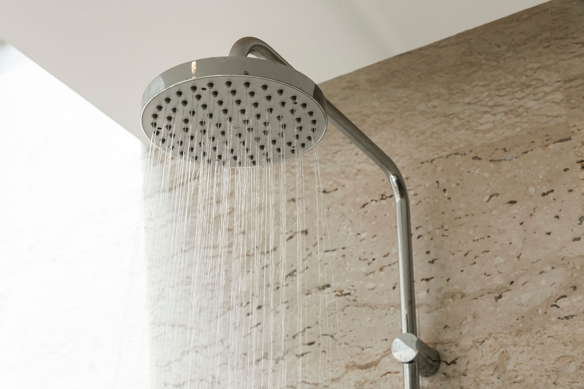 Modern showerhead running water against a beige tiled bathroom wall