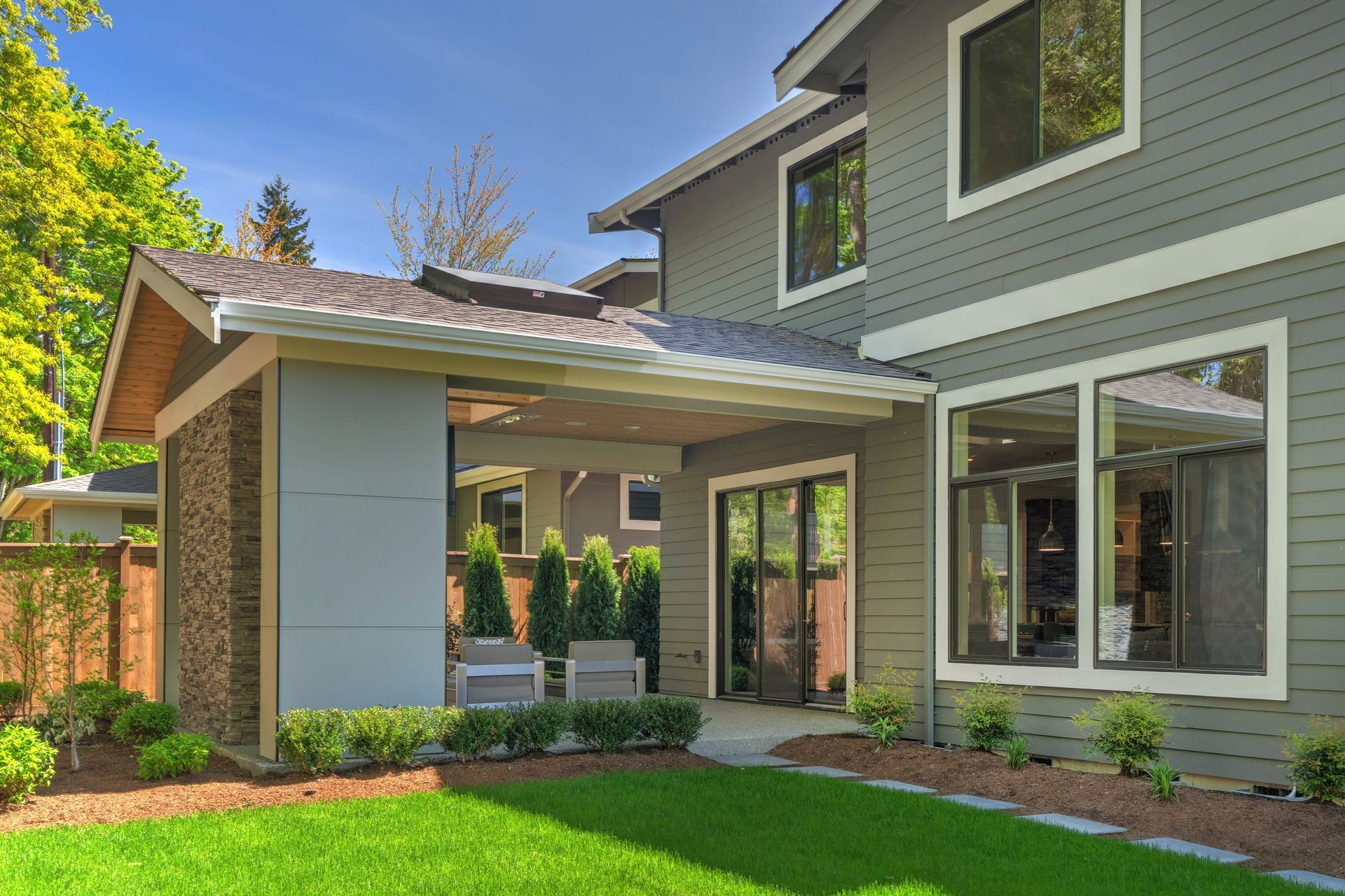 Modern two-story gray house with covered porch, large windows, and a green front lawn Modern two-story gray house with covered porch, large windows, and a green front lawn
