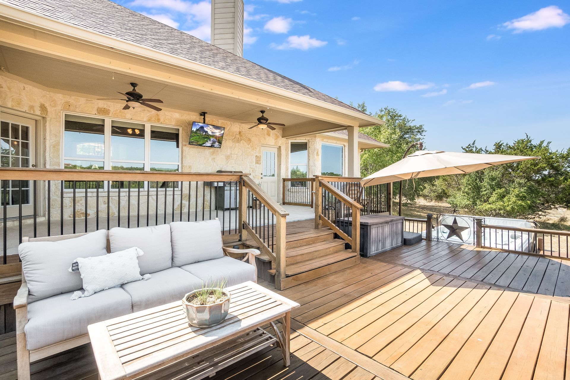 Spacious wooden deck with white outdoor sofas, stairs, and a patio umbrella beside a house under a sunny sky Spacious wooden deck with white outdoor sofas, stairs, and a patio umbrella beside a house under a sunny sky