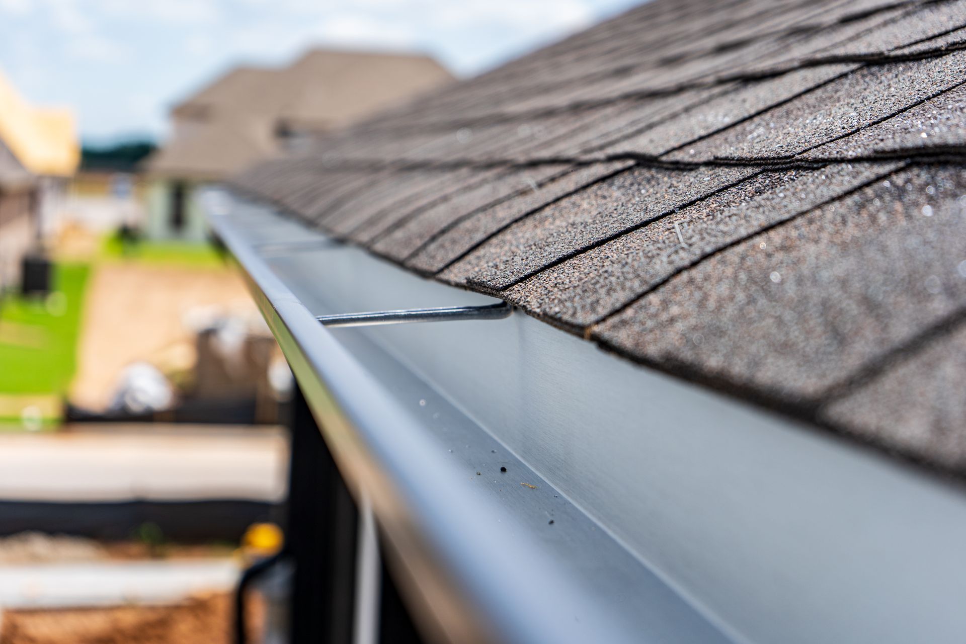 Close-up of a gray metal roof gutter along the edge of a shingled house
