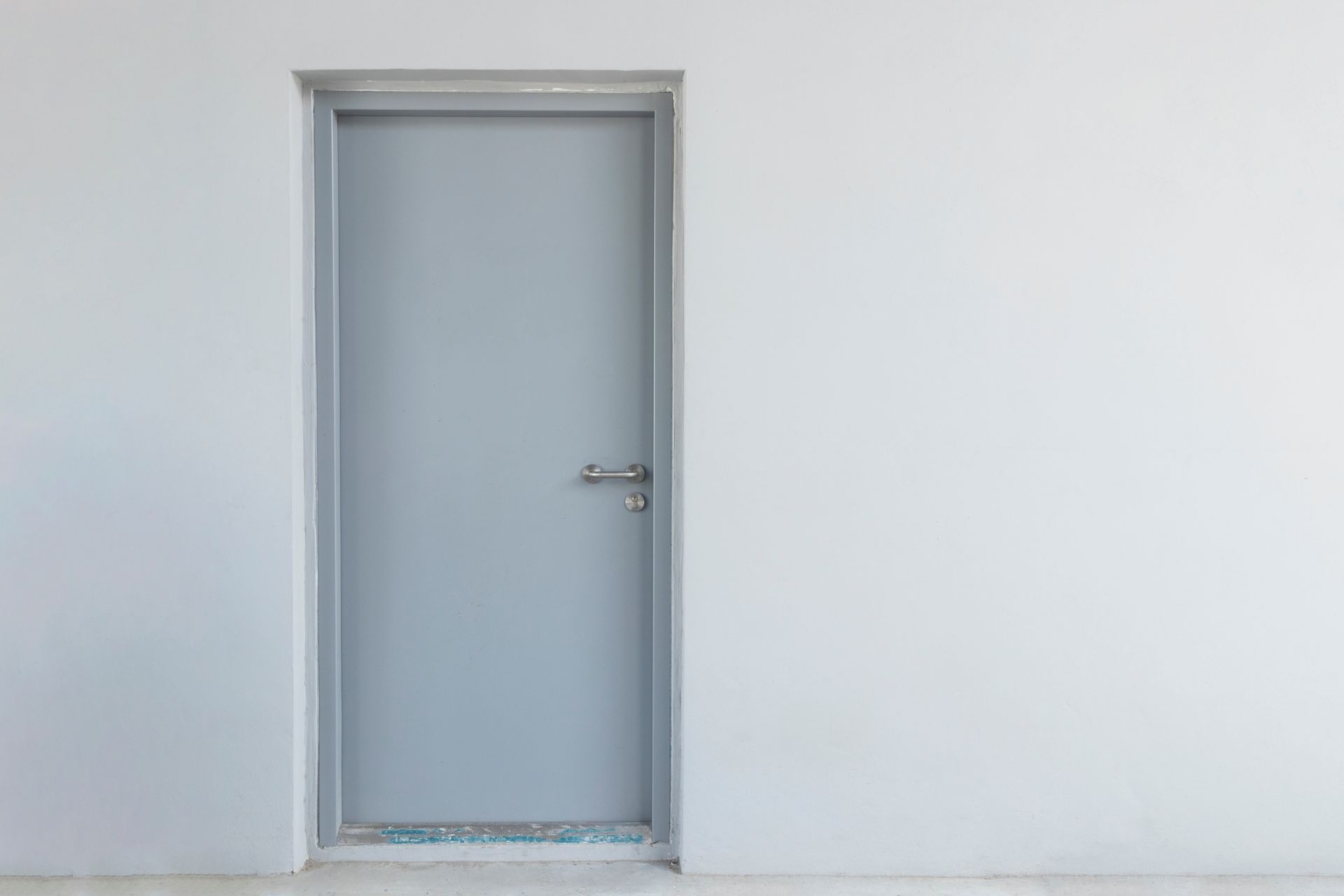 Closed gray door in a white wall with a silver handle and a small floor strip at the base Closed gray door in a white wall with a silver handle and a small floor strip at the base