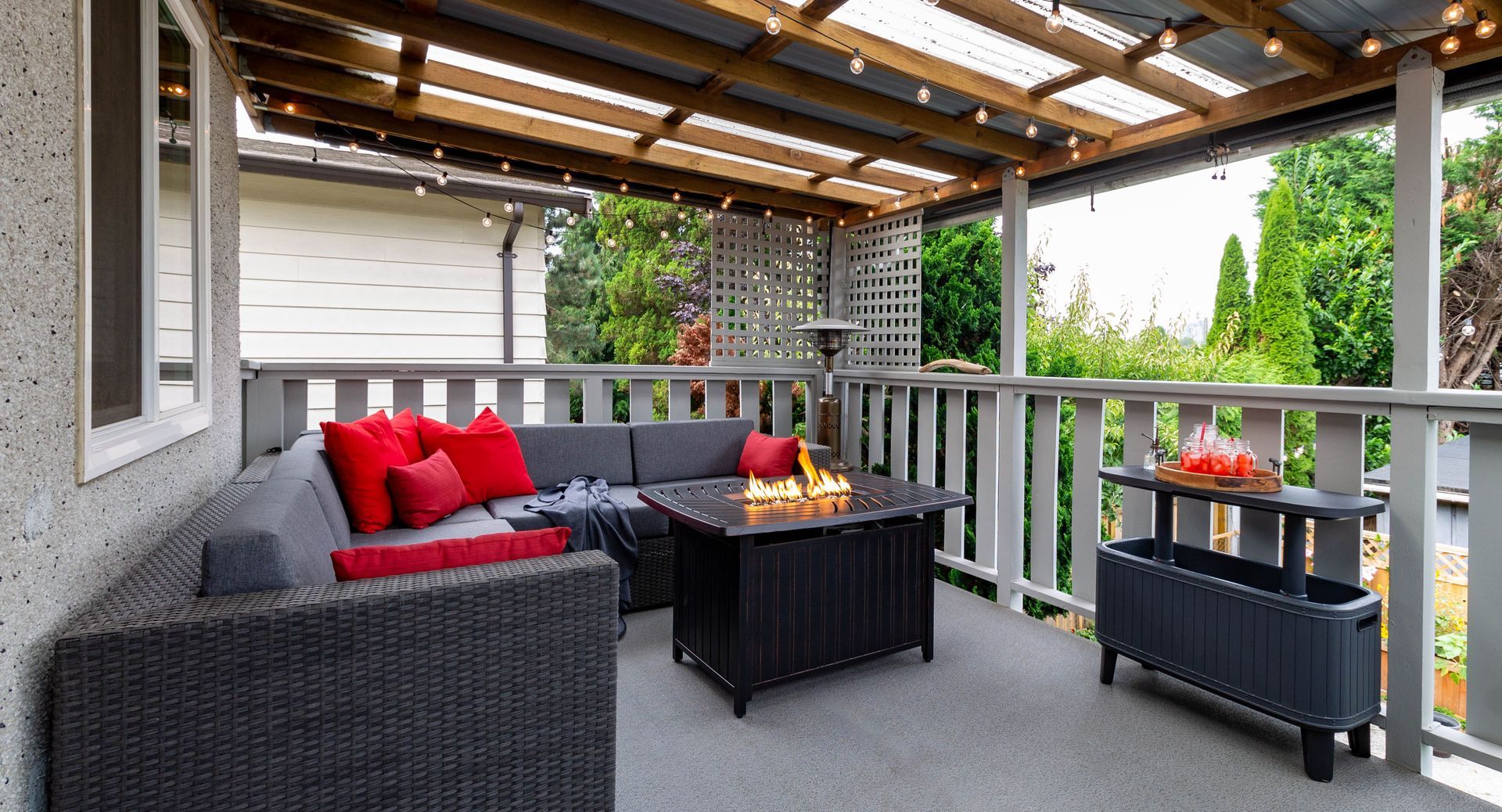 Covered patio with gray wicker sofa, red cushions, coffee table, and potted plants Covered patio with gray wicker sofa, red cushions, coffee table, and potted plants
