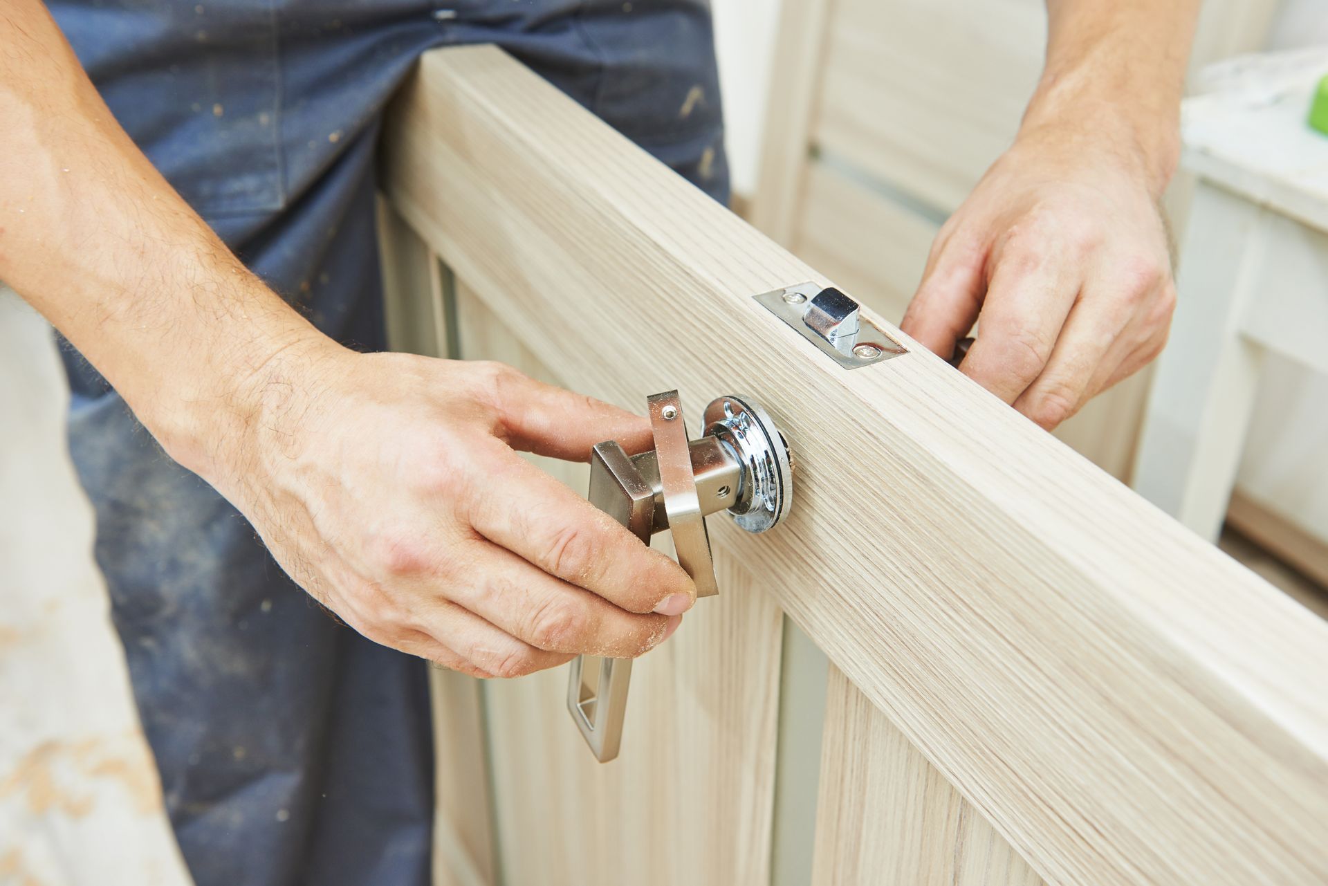 Hands installing a shiny latch on a light wood door panel