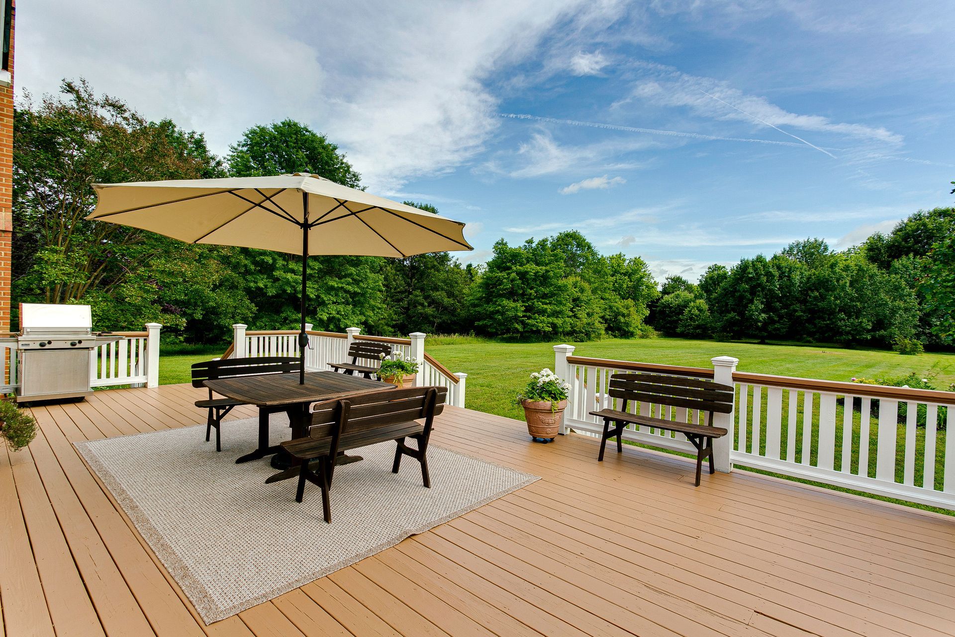 Deck with patio table, umbrella, grill, and potted plants overlooking a green backyard and lake. Deck with patio table, umbrella, grill, and potted plants overlooking a green backyard and lake.