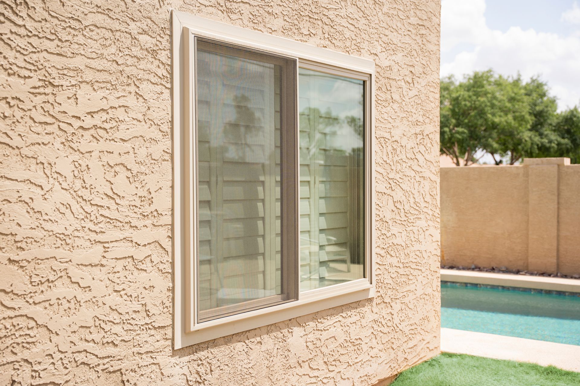 Exterior wall with a window beside a swimming pool and beige privacy fence Exterior wall with a window beside a swimming pool and beige privacy fence
