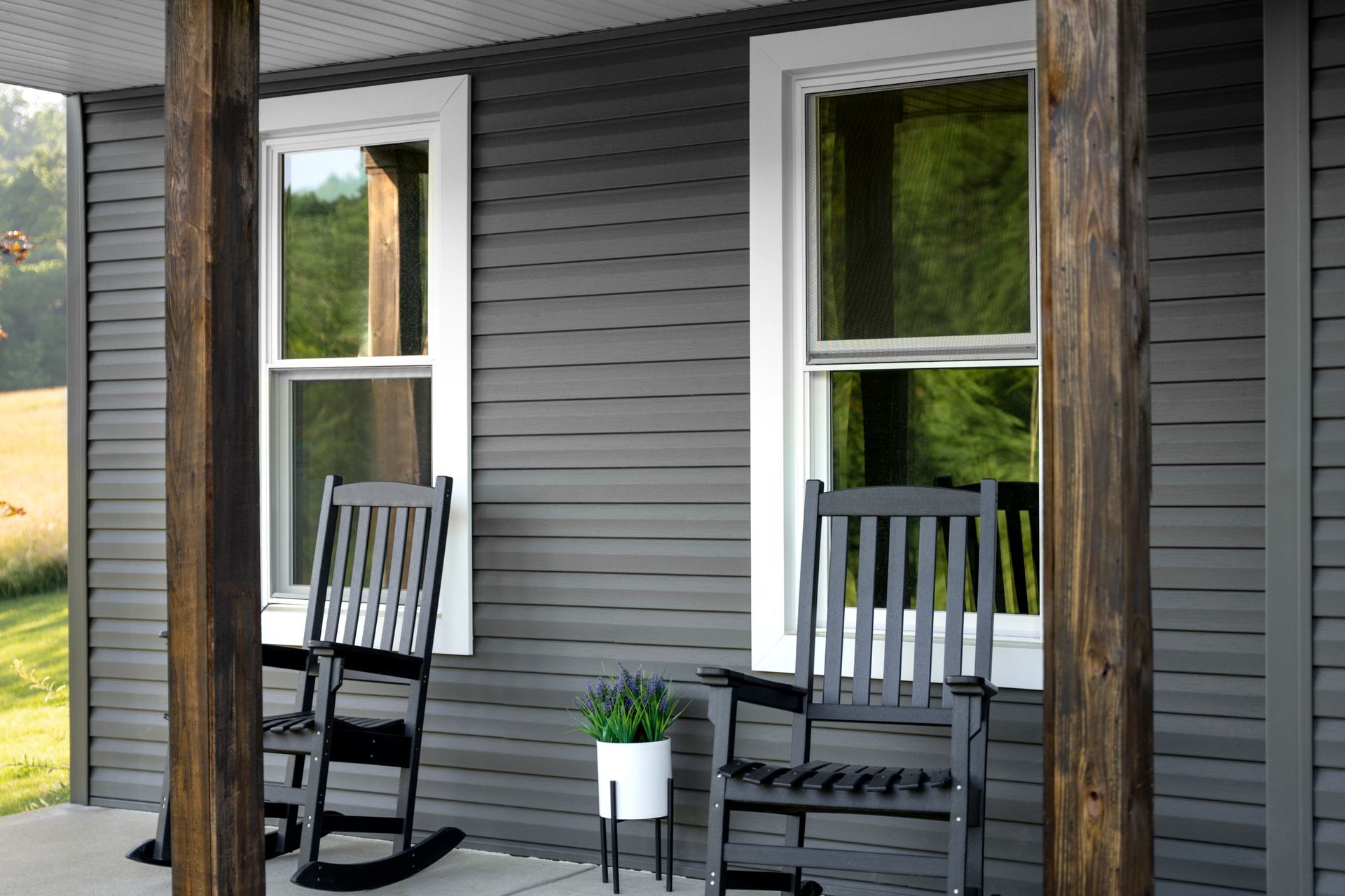 Porch with two black rocking chairs, a small potted plant, and gray siding beside windows Porch with two black rocking chairs, a small potted plant, and gray siding beside windows