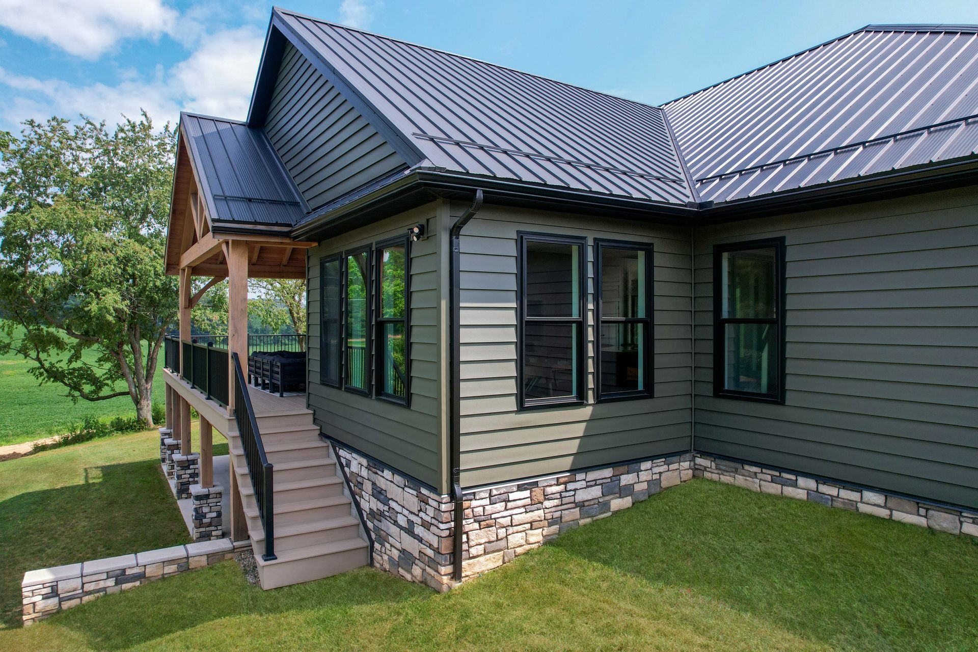 Modern house exterior with dark metal roof, stone base, and covered porch on a grassy lawn Modern house exterior with dark metal roof, stone base, and covered porch on a grassy lawn