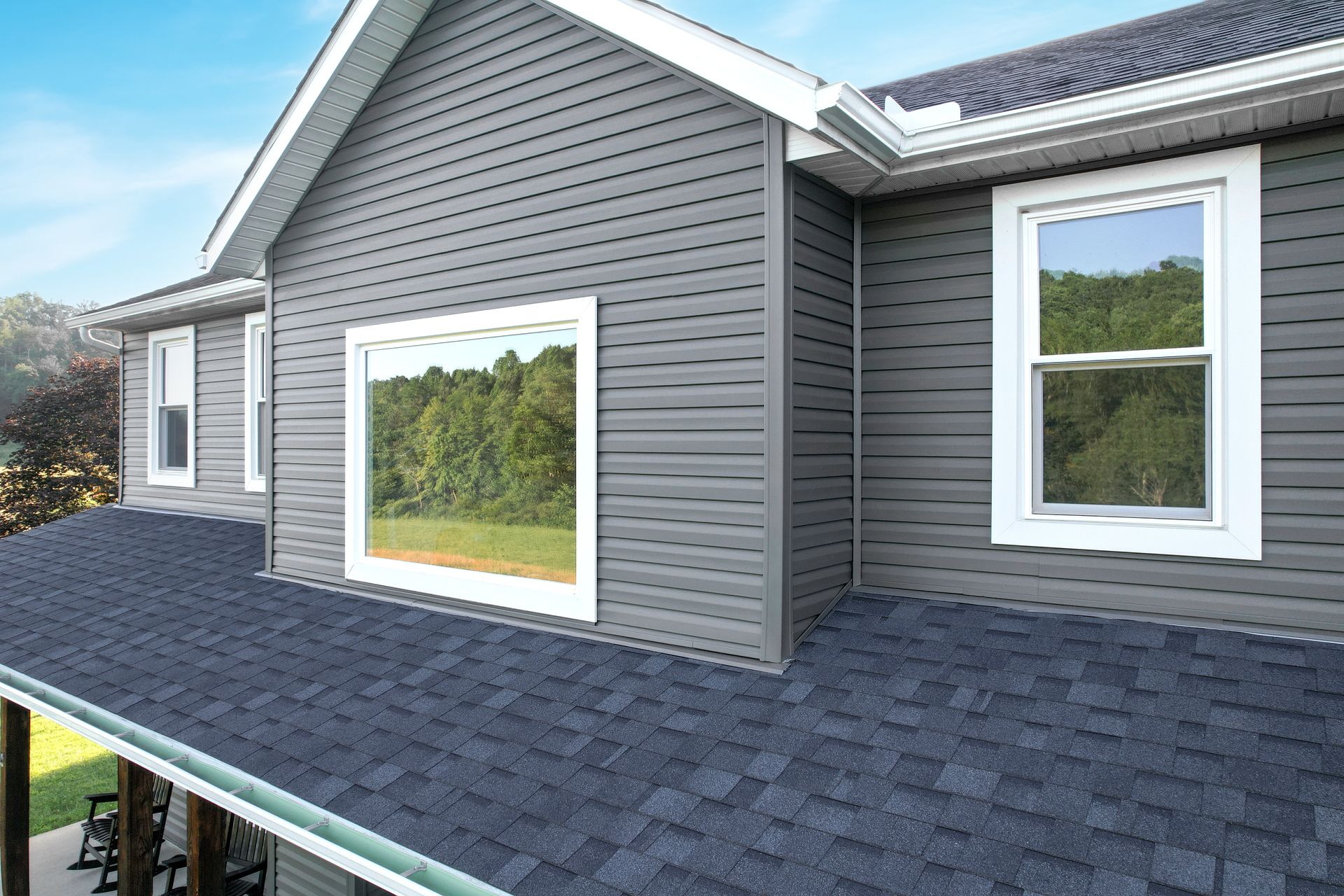 Gray house exterior with shingled roof and white-trimmed windows under a blue sky Gray house exterior with shingled roof and white-trimmed windows under a blue sky
