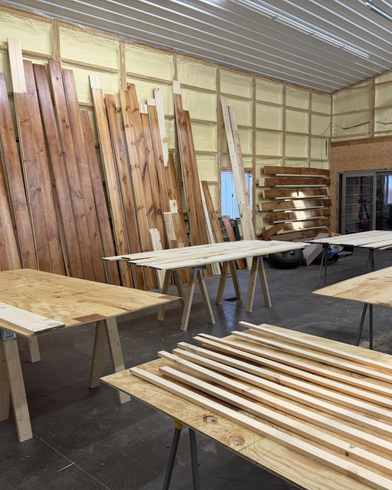 Workshop with stacks of unfinished wooden boards and benches inside a large storage space