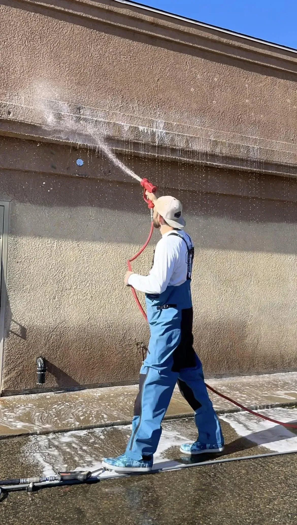 A man is cleaning the side of a building with a hose.