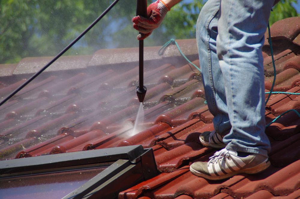 A person is cleaning a tiled roof with a high pressure washer.