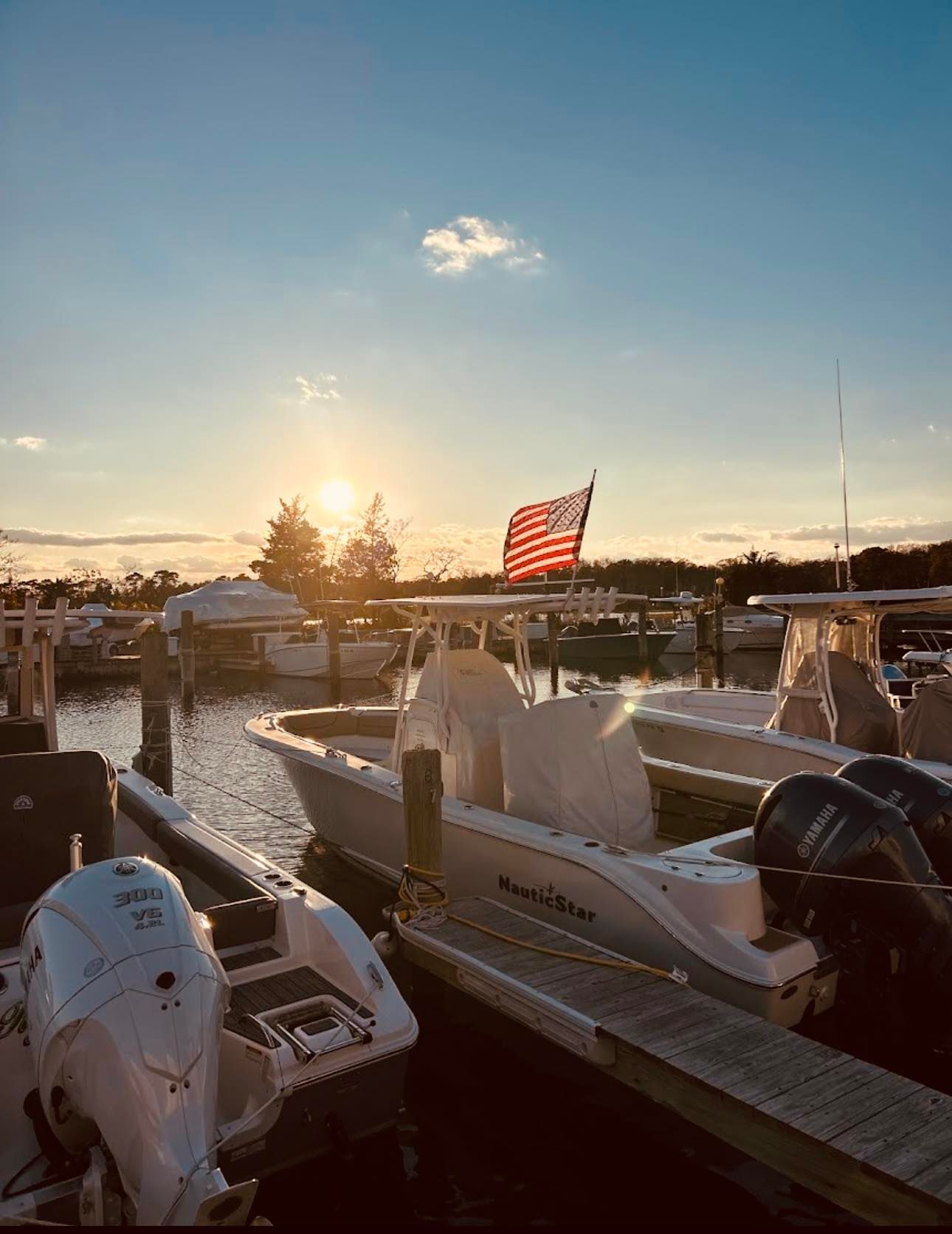 Sunset over a marina with docked boats and an American flag waving