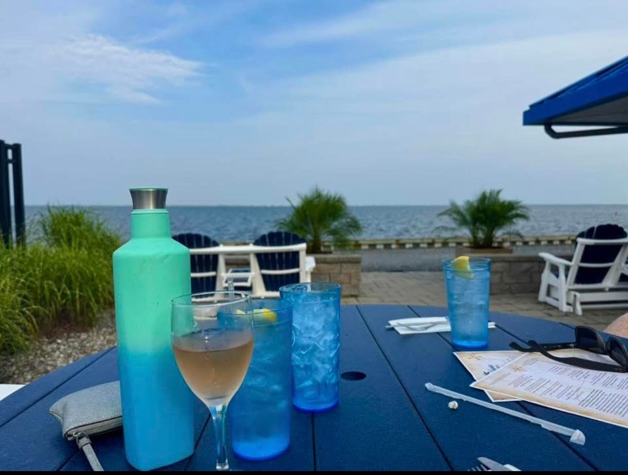 Blue drinks on a seaside patio table with ocean view and lounge chairs.